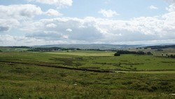 The best prospect of the battlefield can be gained from the minor road leading up past Greenchesters and Holt Wood. This view is looking south eastward down Redesdale towards Otterburn. The original site of the Percy Cross was in the centre of the nearest light green field on the flat ground to the left of the plantation in the middle distance.